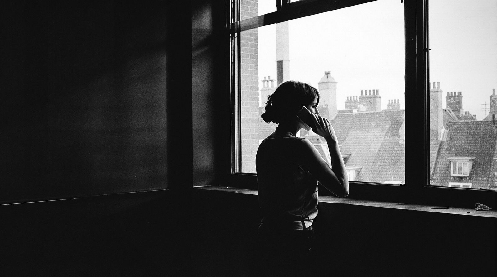 Frau am Fenster telefoniert, Blick über Dächer