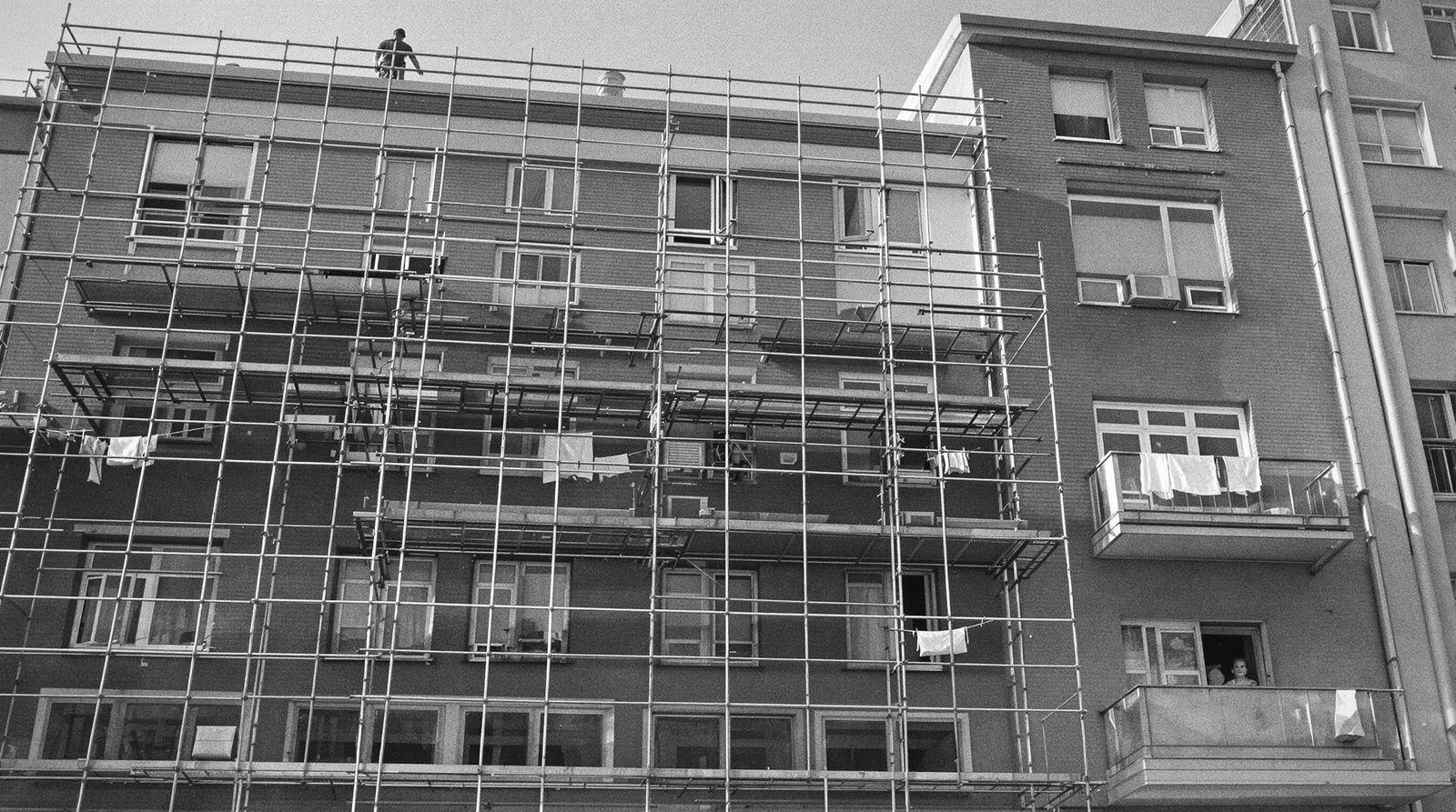 Gerüst an einem bewohnten Mehrfamilienhaus, oben ein Dachdecker