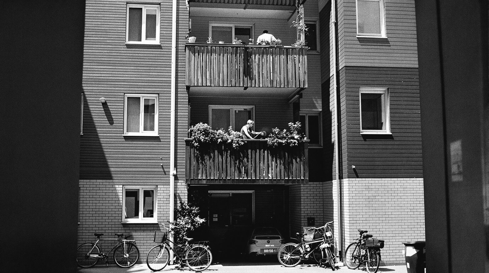 Innenhof eines Mehrfamilienhauses, auf einem Balkon gießt jemand Pflanzen