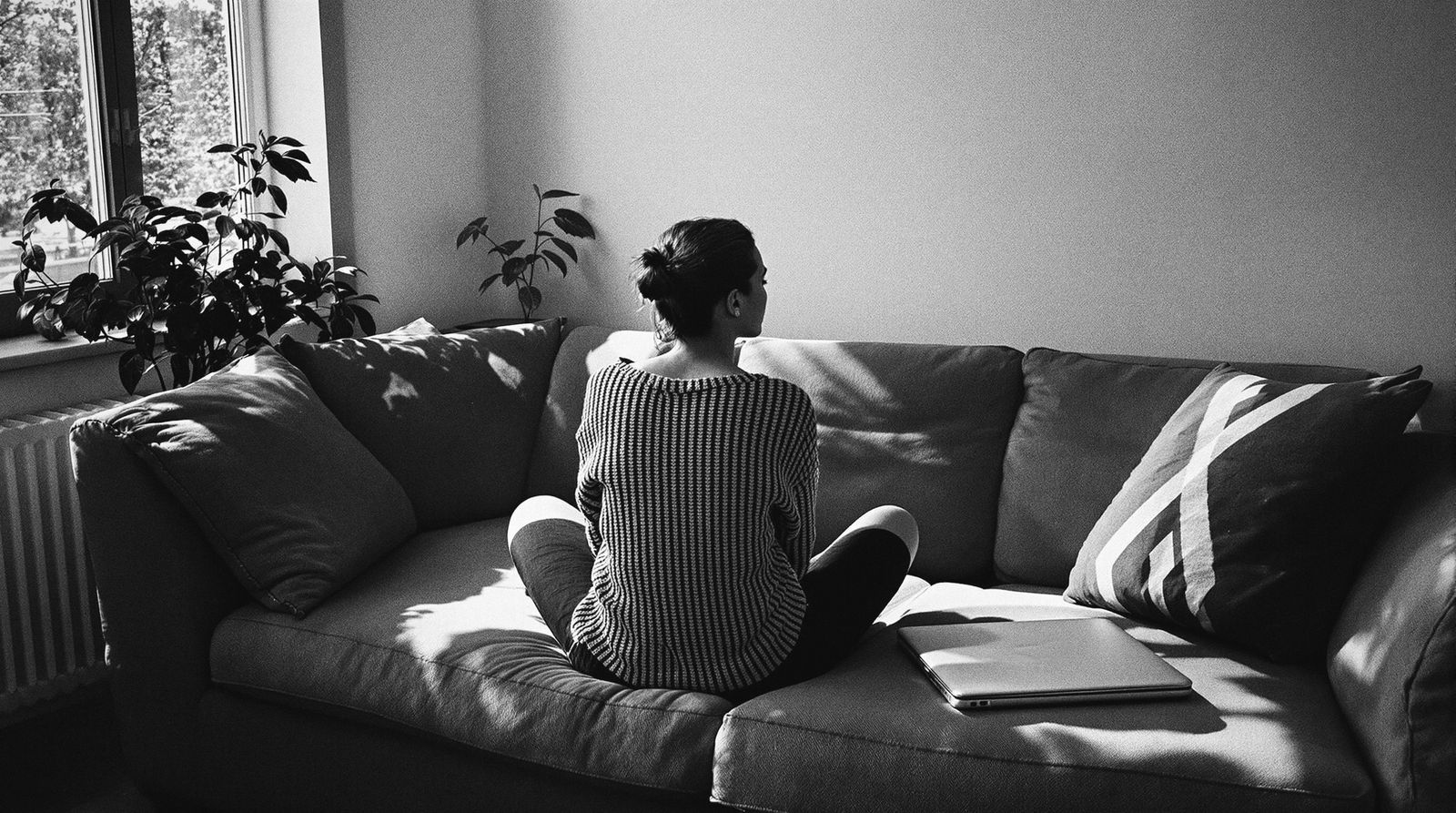 Eine junge Frau sitzt im Schneidersitz auf dem Sofa, der zugeklappte Laptop liegt neben ihr