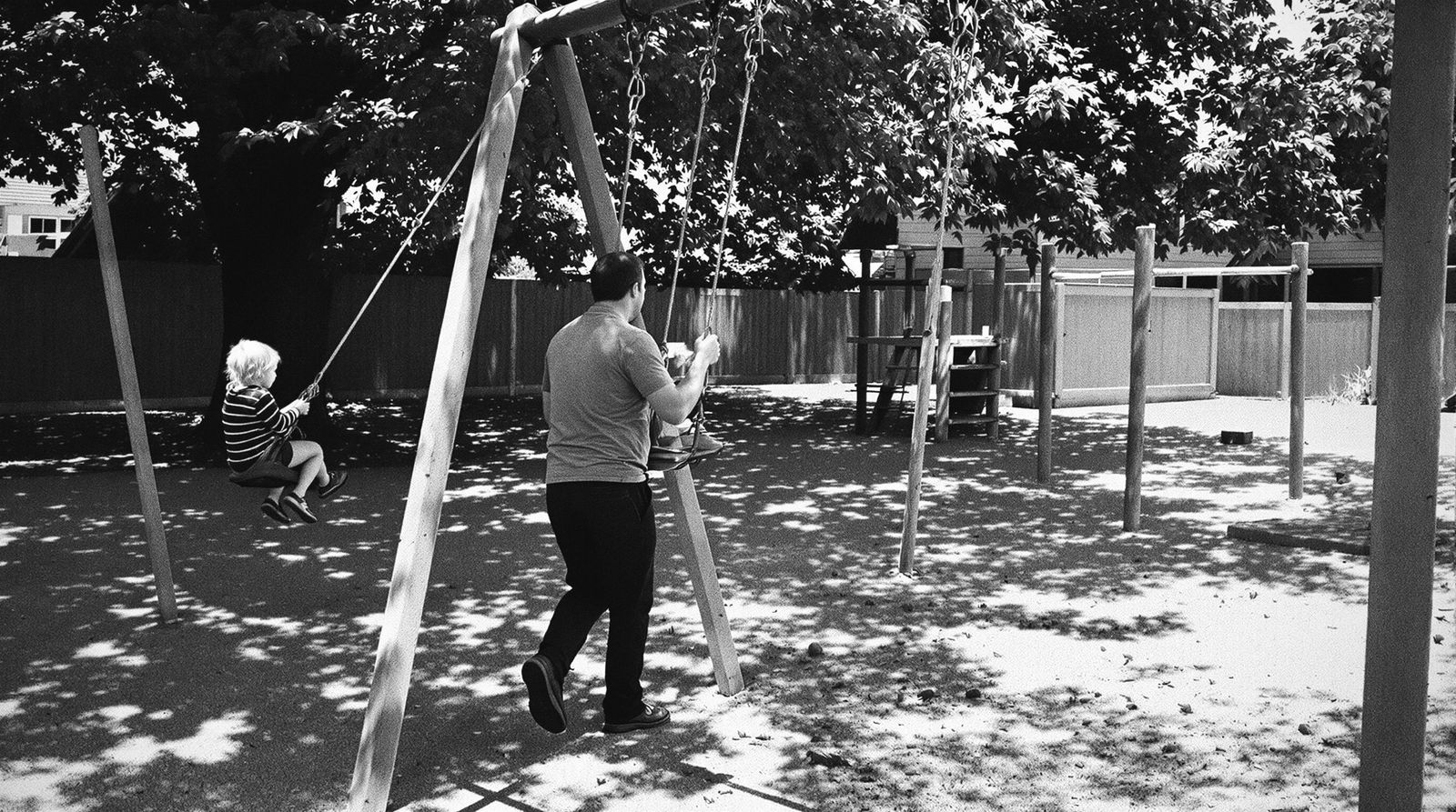 Ein Vater schubst ein kleines Kind auf der Schaukel eines Spielplatzes an