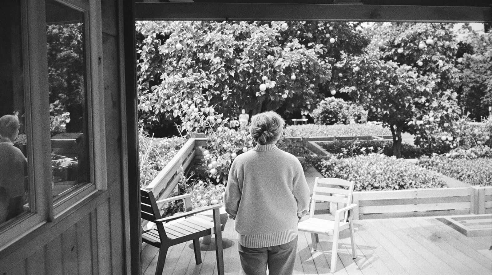 Eine Frau steht auf der Gartenterrasse und blickt über den Nutzgarten, von hinten gesehen